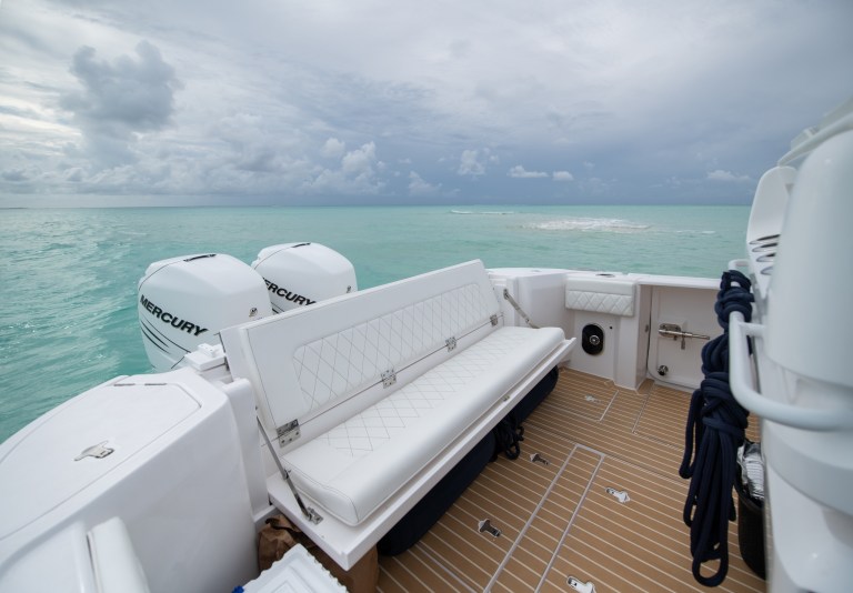 View from a boat with white seating and engines, overlooking calm, turquoise waters and a cloudy sky.