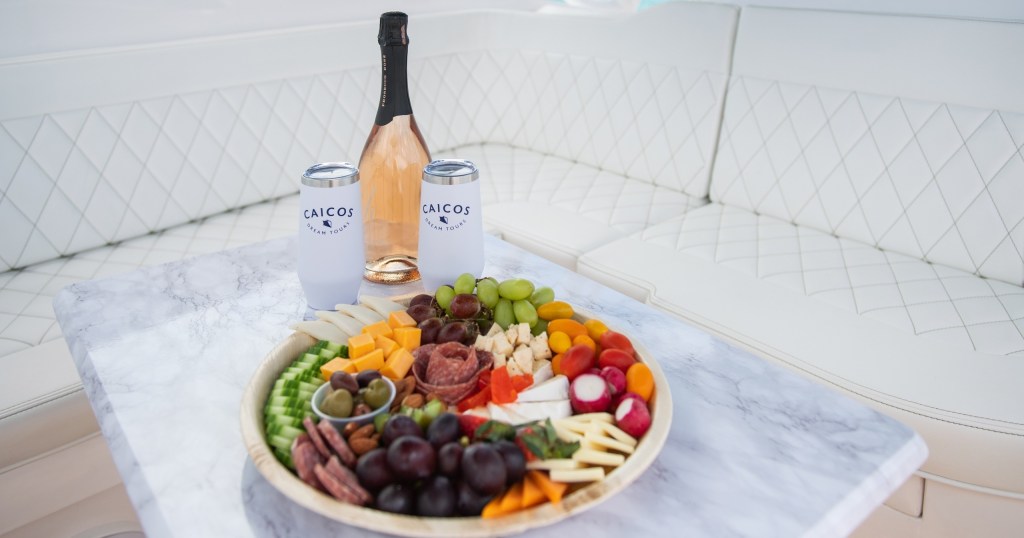 Plate of fruits, nuts, and cheese with two cans and a bottle on a boat seating.