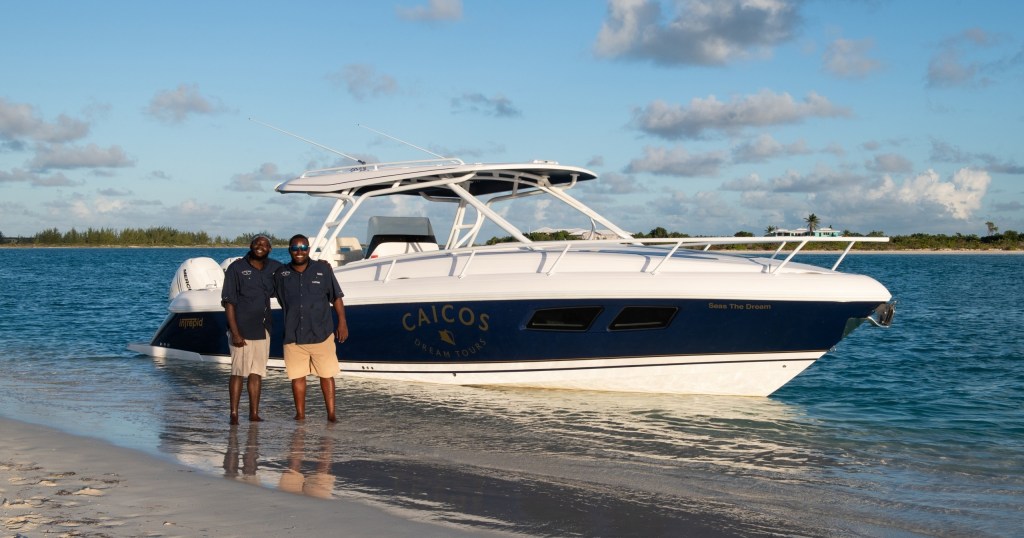 Two people standing on a beach beside a white and blue powerboat.