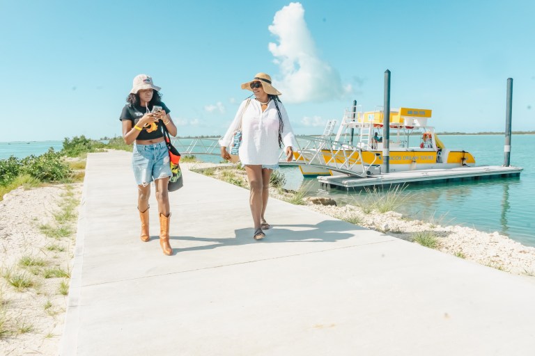 Two women walking on a path near water, with a boat in the background.