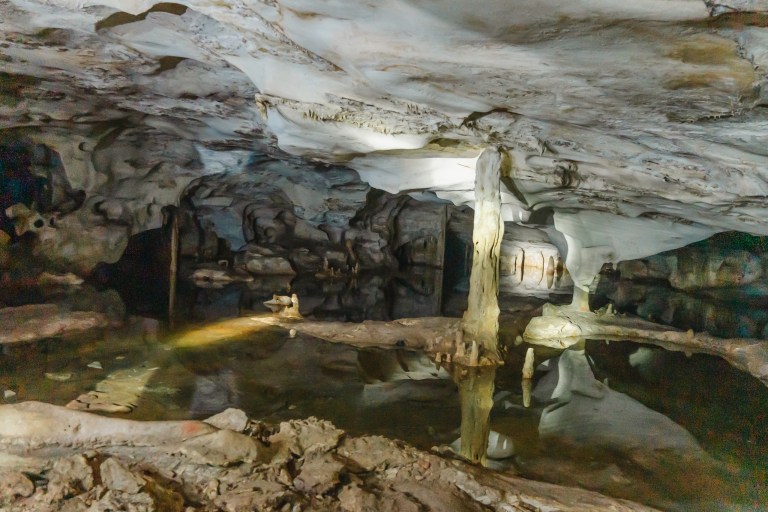 Underground cave with stalactites, stalagmites, and a reflective pool.