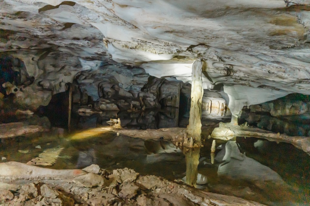 Underground cave with stalactites, stalagmites, and a reflective pool.