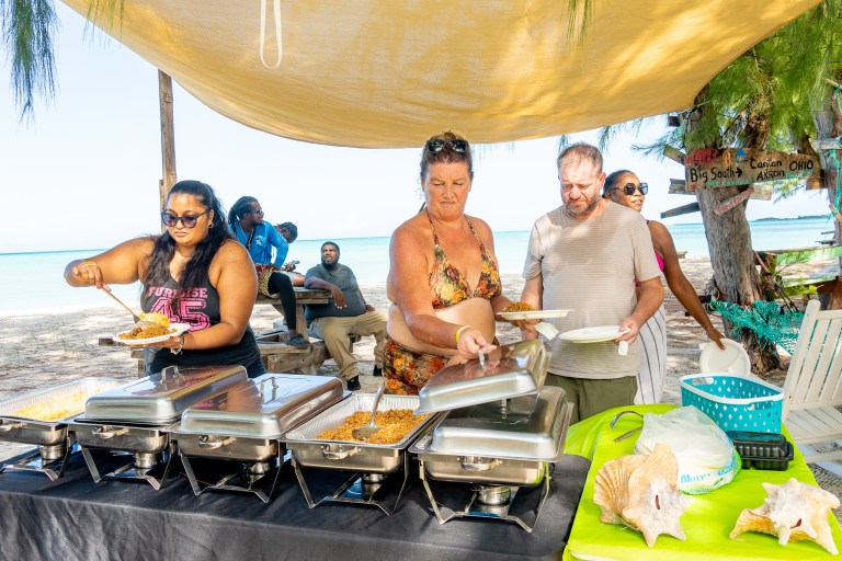 People serving buffet food at an outdoor beach picnic.