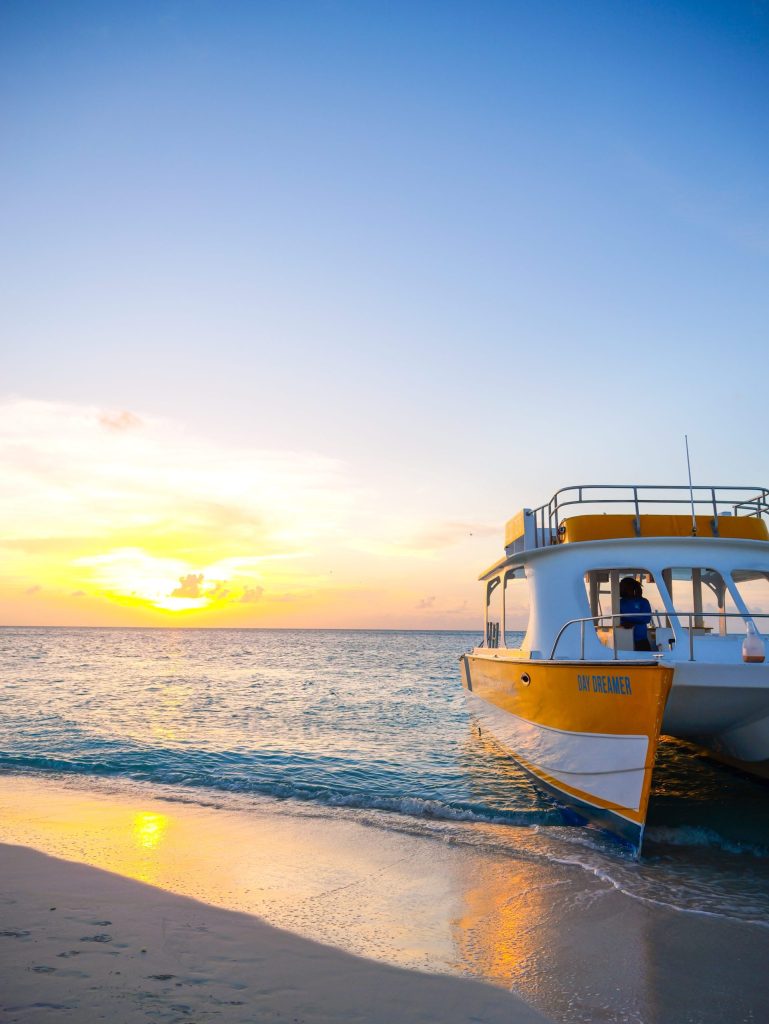 Boat on beach at sunset with calm sea and clear sky.