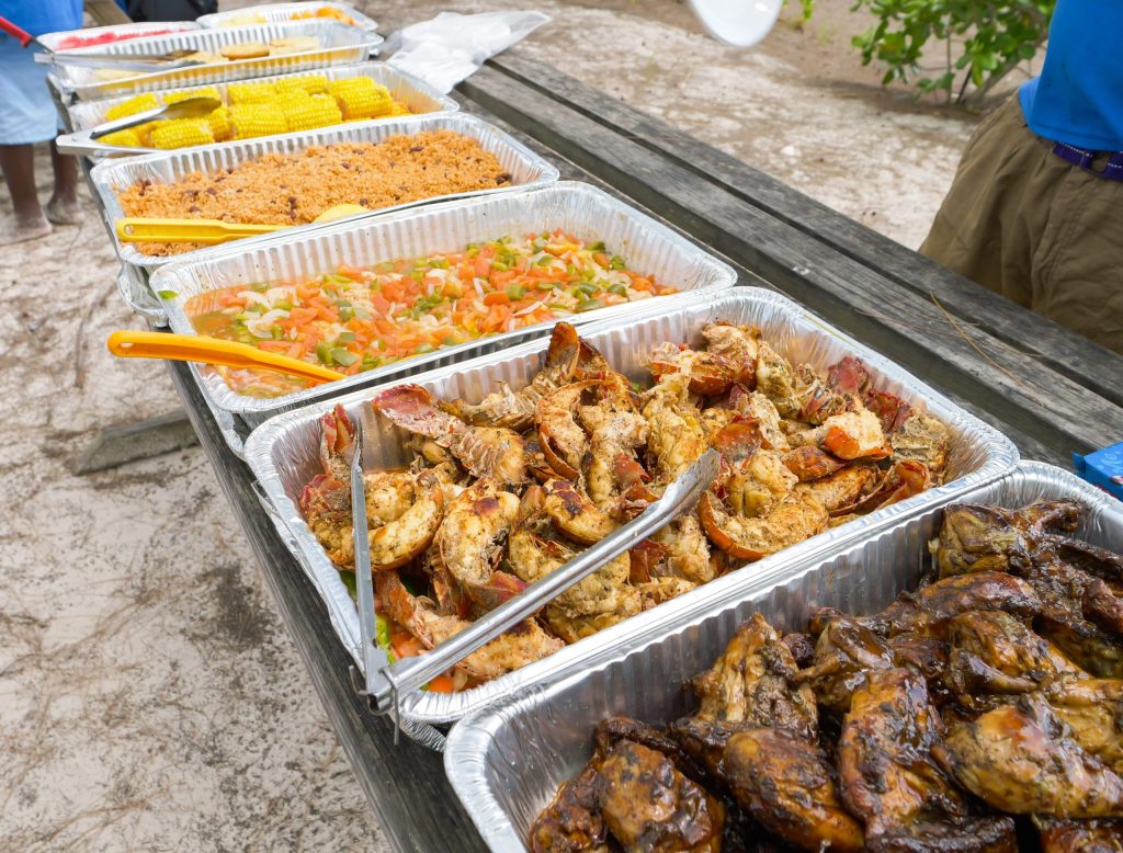 Buffet table outdoors with trays of seafood, vegetables, rice, corn, and meat.