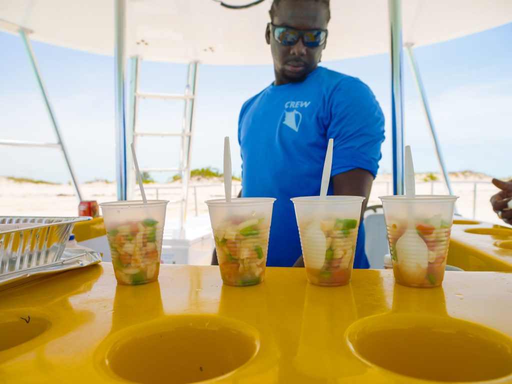 Person with four cups of diced fruit on a yellow surface in a sunny outdoor setting.