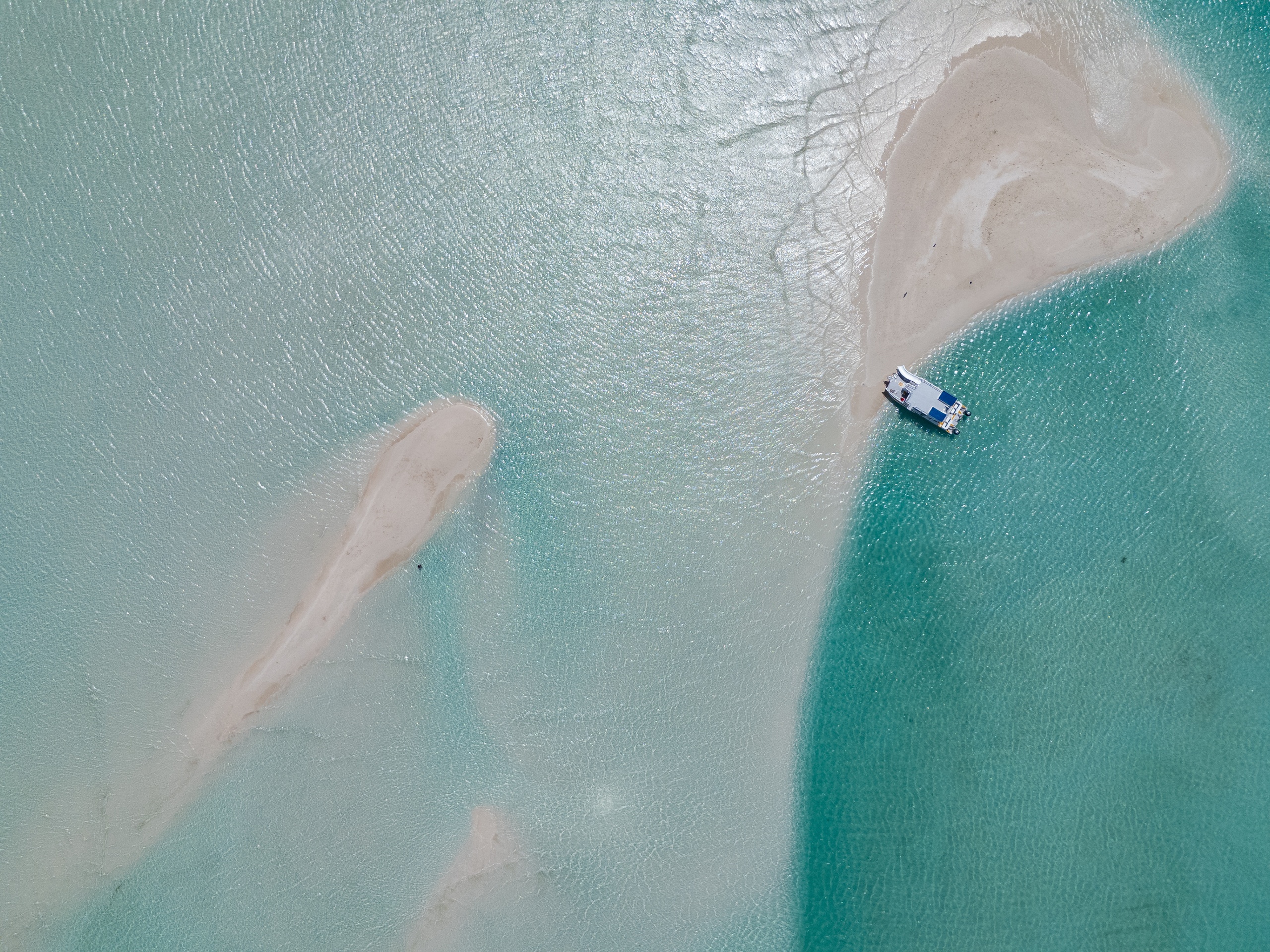 Aerial view of a boat on turquoise water near sandy beaches.