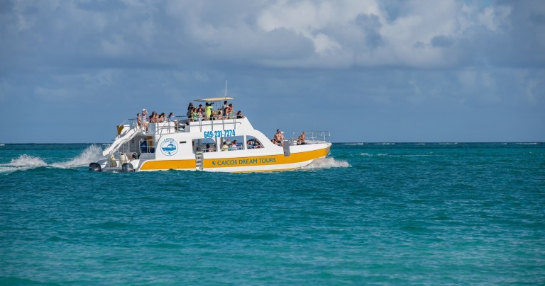 Tour boat with people cruising on turquoise ocean water under cloudy sky.