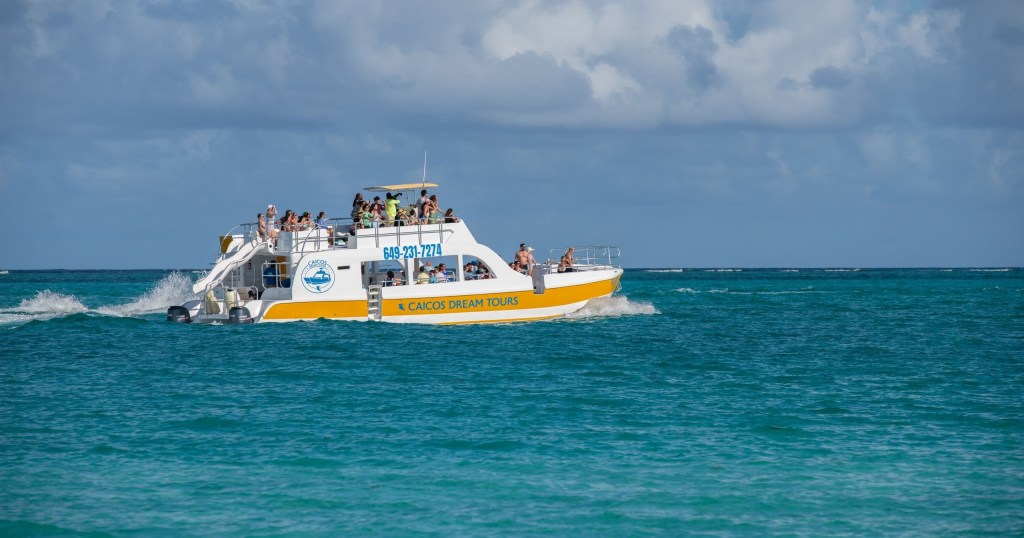 Tour boat with people cruising on turquoise ocean water under cloudy sky.