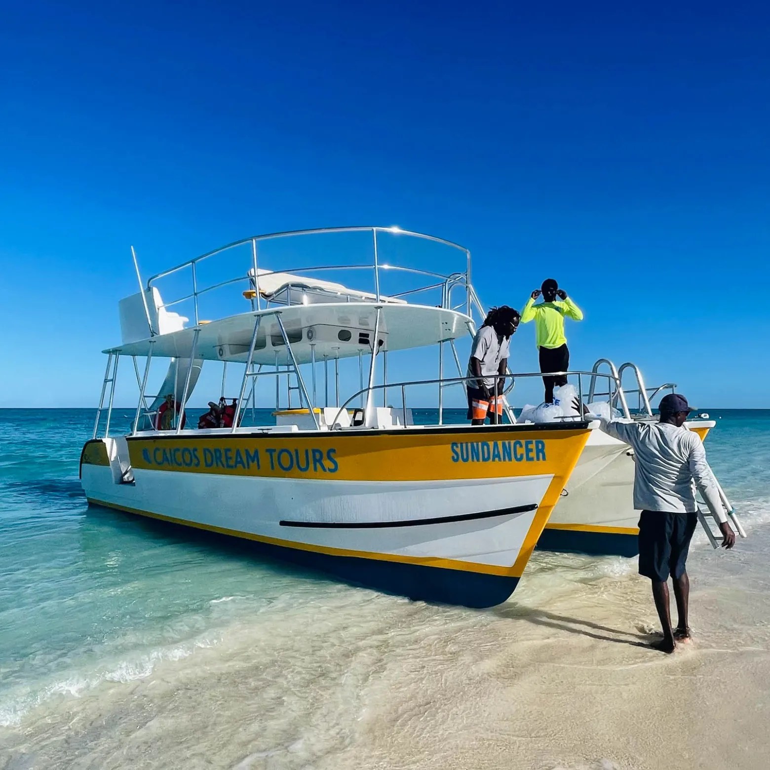 Boat on sandy beach with clear blue sky, three people onboard.