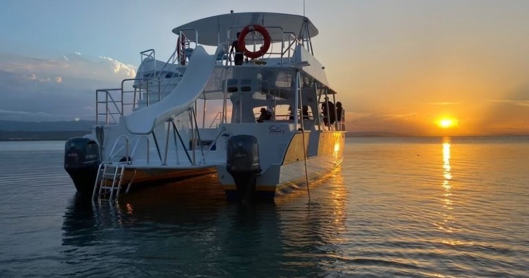 Boat with slide on lake at sunset.