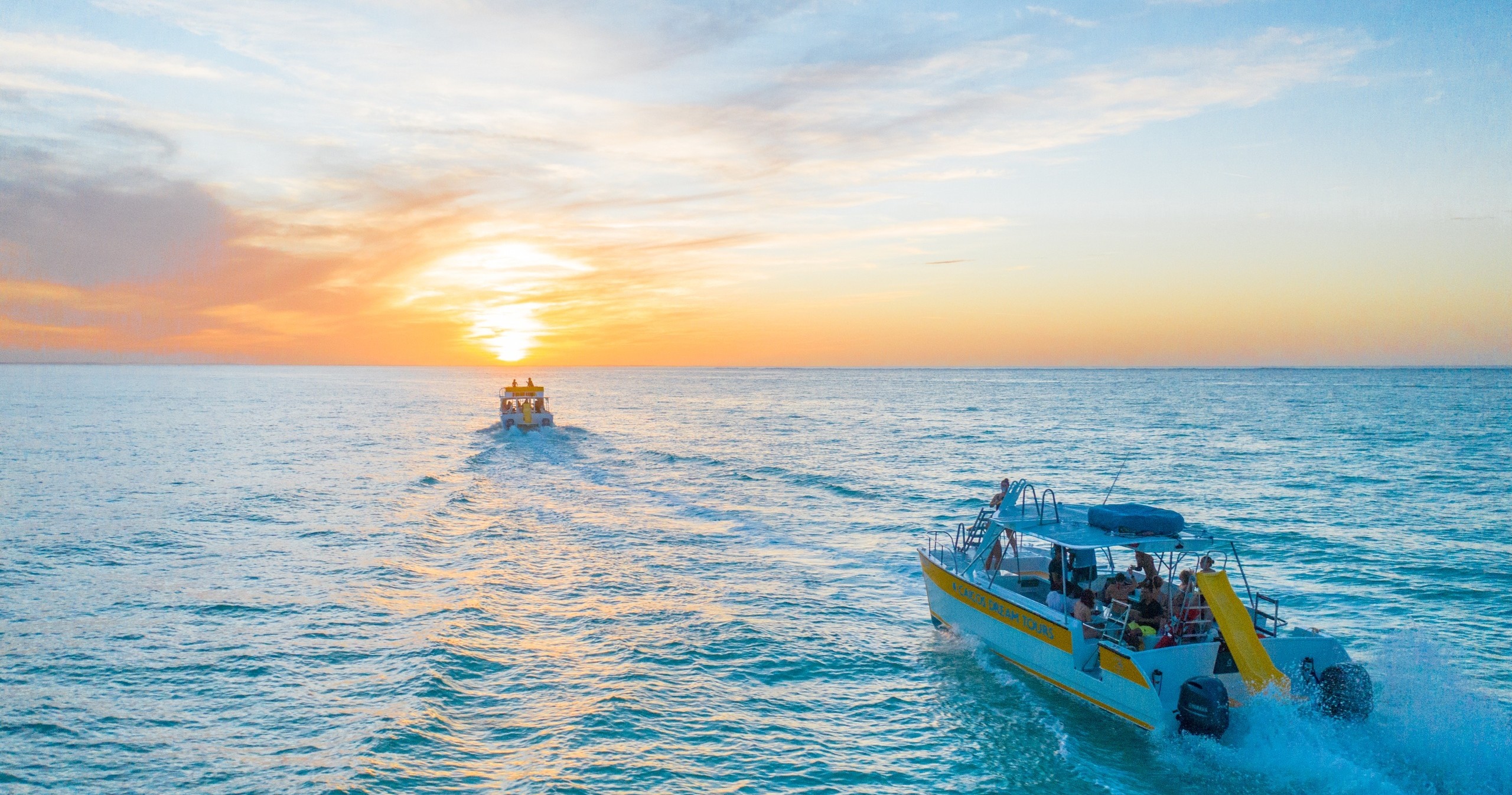 Two boats sailing towards sunset on the ocean.