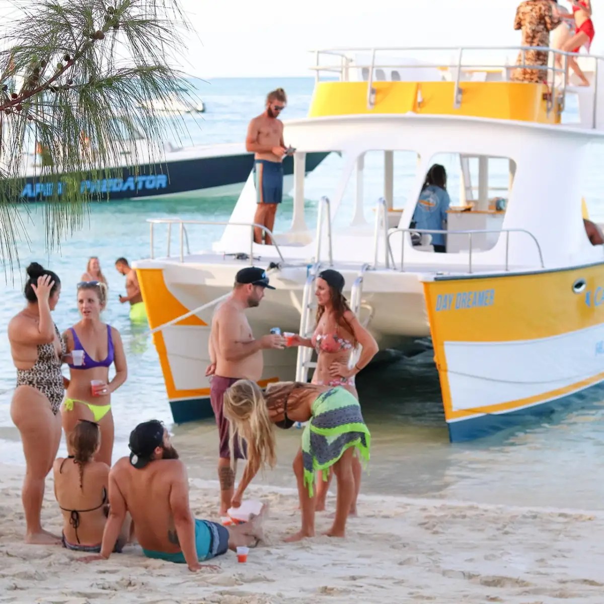 Group of people socializing on a beach near a boat.
