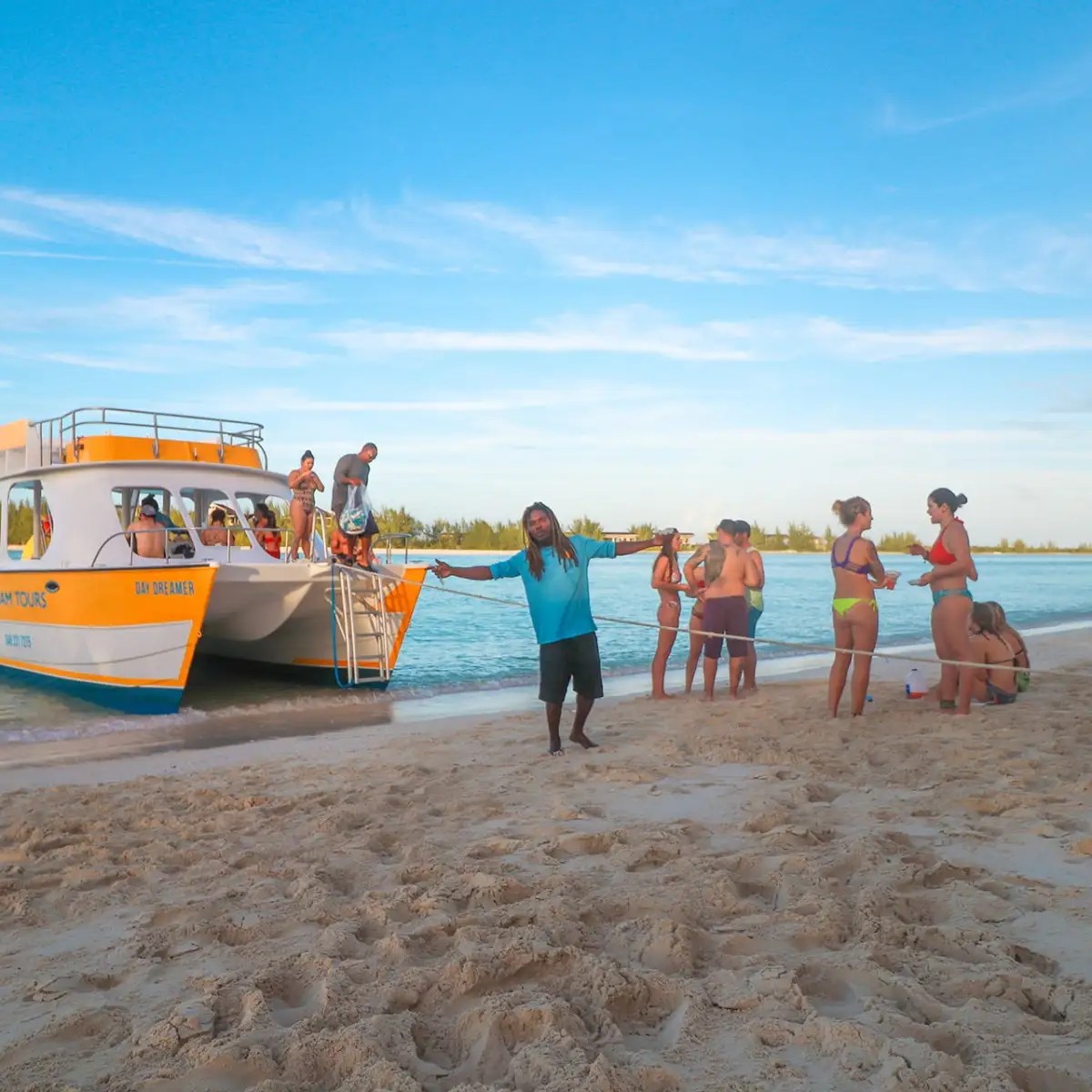 People on a sandy beach near a boat under a clear blue sky.