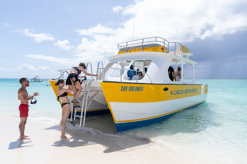 People boarding a yellow and white boat named Day Dreamer on a sunny beach.