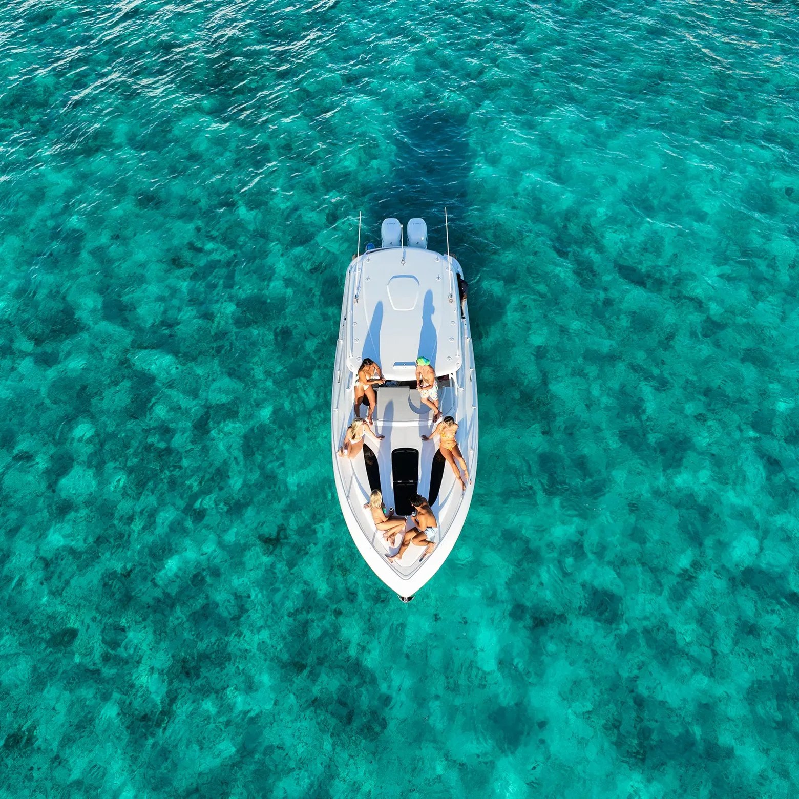 Aerial view of people relaxing on a boat in clear turquoise water.