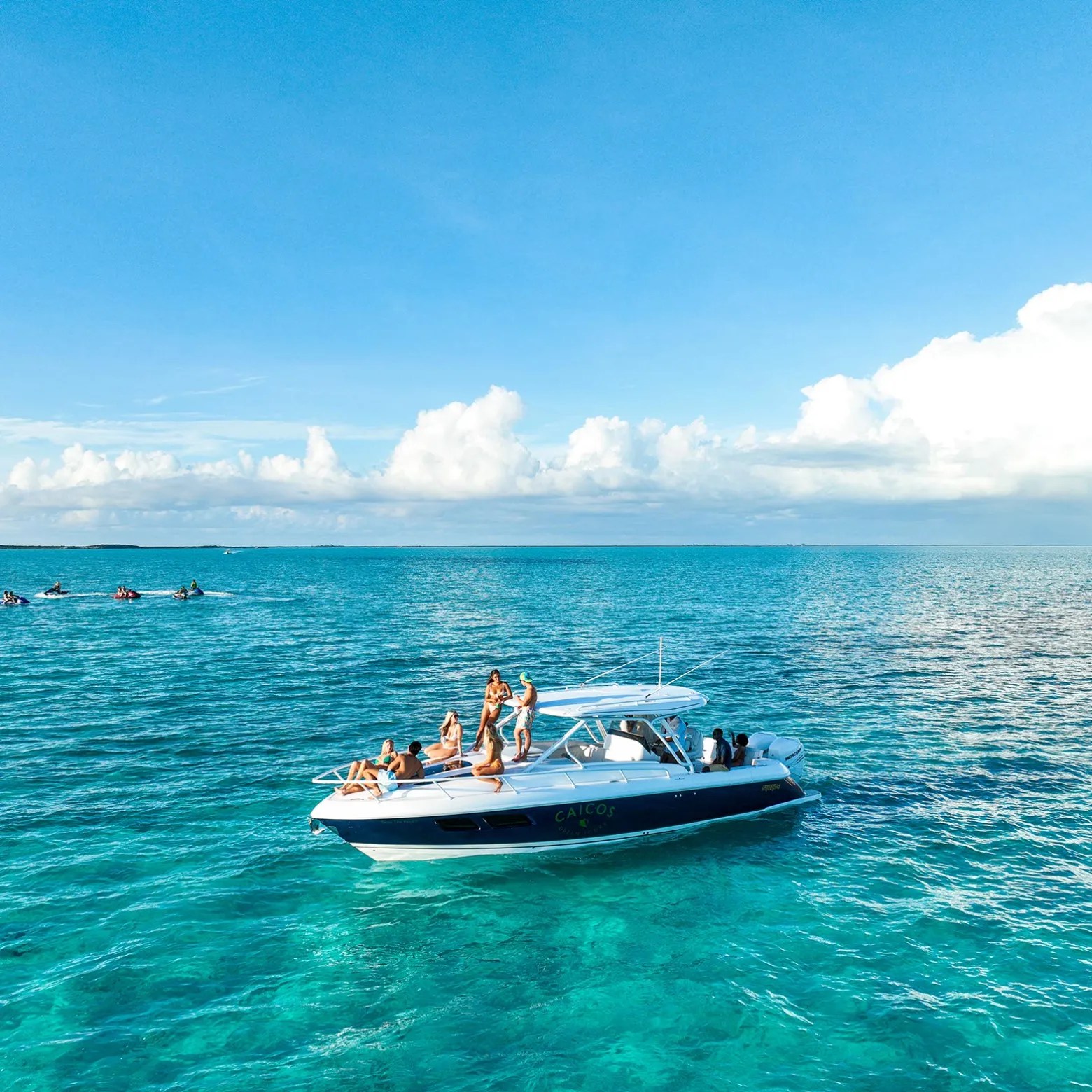A group of people enjoying a sunny day on a boat in clear, blue ocean waters.