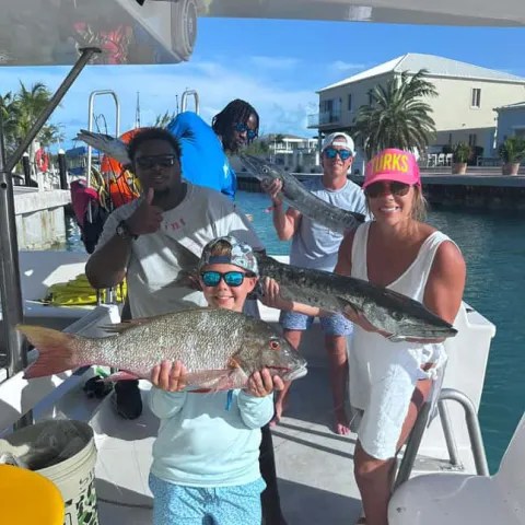 Group of five people on a boat holding large fish, smiling.