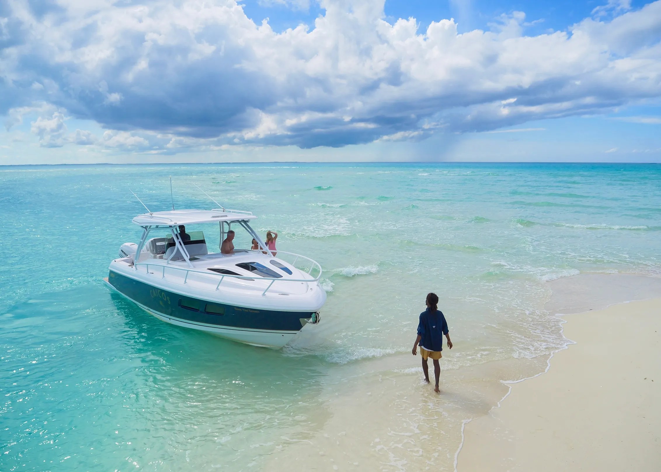 Person walking on beach towards docked motorboat under cloudy sky.