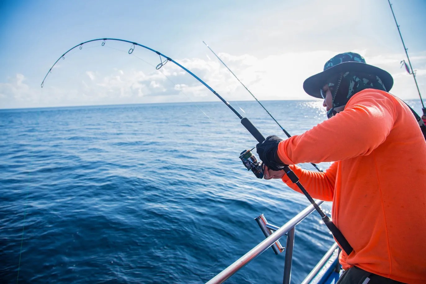 Person in a hat reeling in a fish on a boat in the ocean.