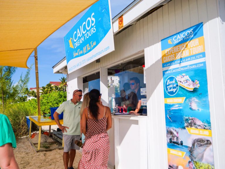 People at a beachside tour booth with colorful signage.
