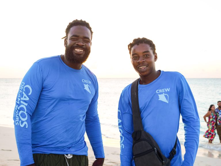 Two people in blue shirts smiling on a beach.