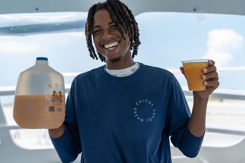 Smiling person holding a jug and cup of orange drink on a boat.