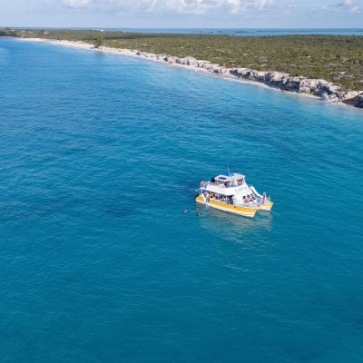 A boat with people near a rocky coastline and blue ocean under a clear sky.