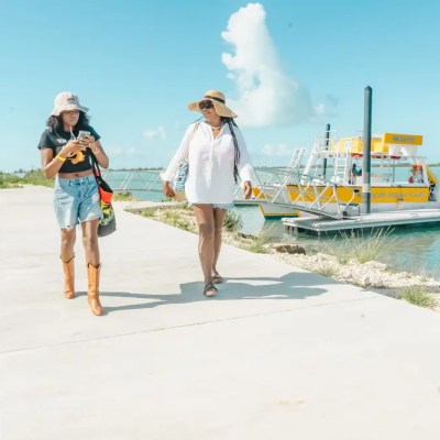 Two women walking on a pier near a boat under a clear blue sky.