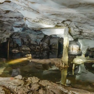 Interior of a cave with stalactites and stalagmites, dimly lit, with reflective water surface.