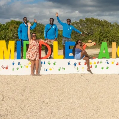 Group posing in front of 'I ❤️ Middle Caicos' sign with handprint art below.