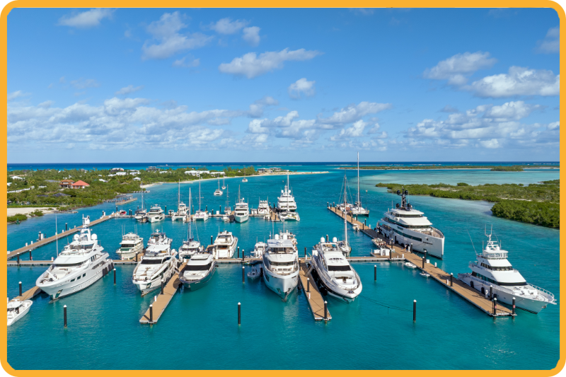 Yachts docked at a marina in turquoise water under a bright blue sky with scattered clouds.